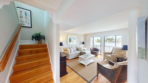 A spacious living room with a staircase, a sofa set, a coffee table, and a view of the outdoors. - Lakeside Updated Villa: Pool and Beach Access (Pawleys Island)