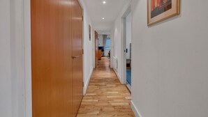 Un couloir avec des portes en bois et un plancher en bois, qui mène à une pièce contenant un lit et une fenêtre.