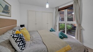 Une chambre à coucher avec un lit, une fenêtre avec des rideaux, une porte et un luminaire au plafond.