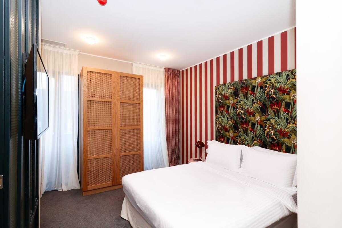 A hotel room with a bed, a wardrobe, a television, and a striped wall.