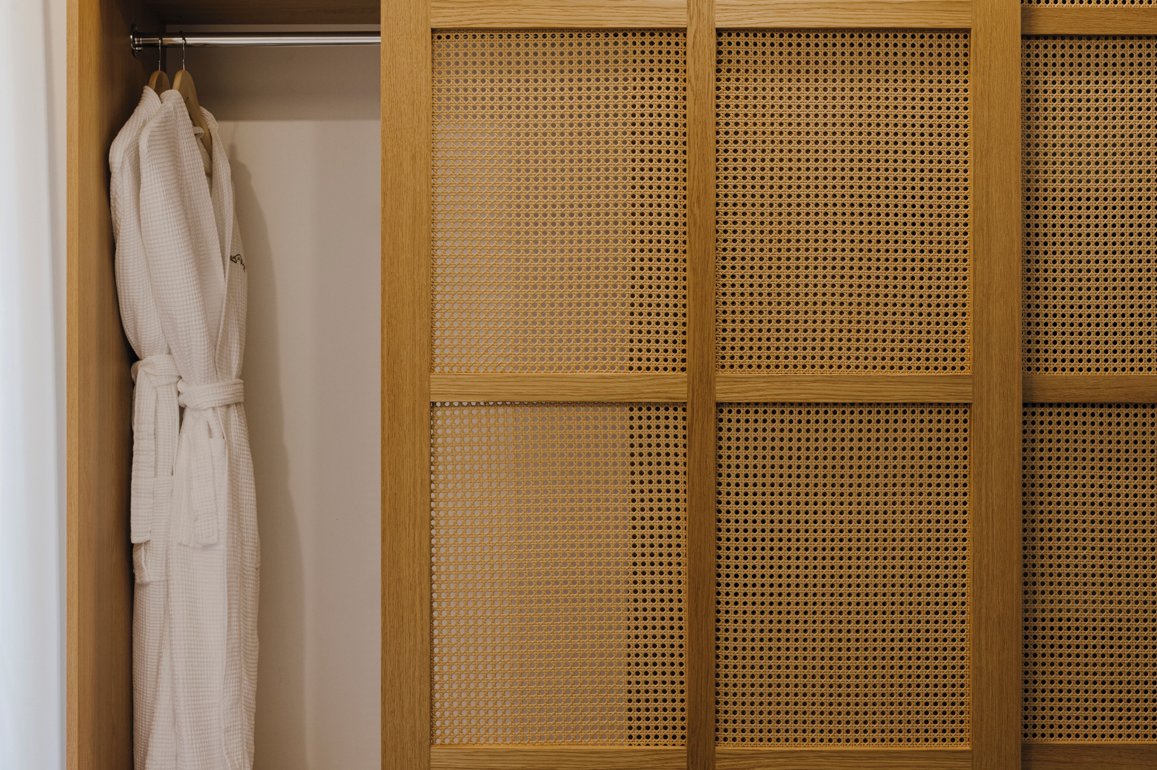 A wooden wardrobe with a woven door, a white robe hanging on the door, and a wooden hanger.