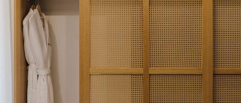 A wooden wardrobe with a woven door, a white robe hanging on the door, and a wooden hanger.