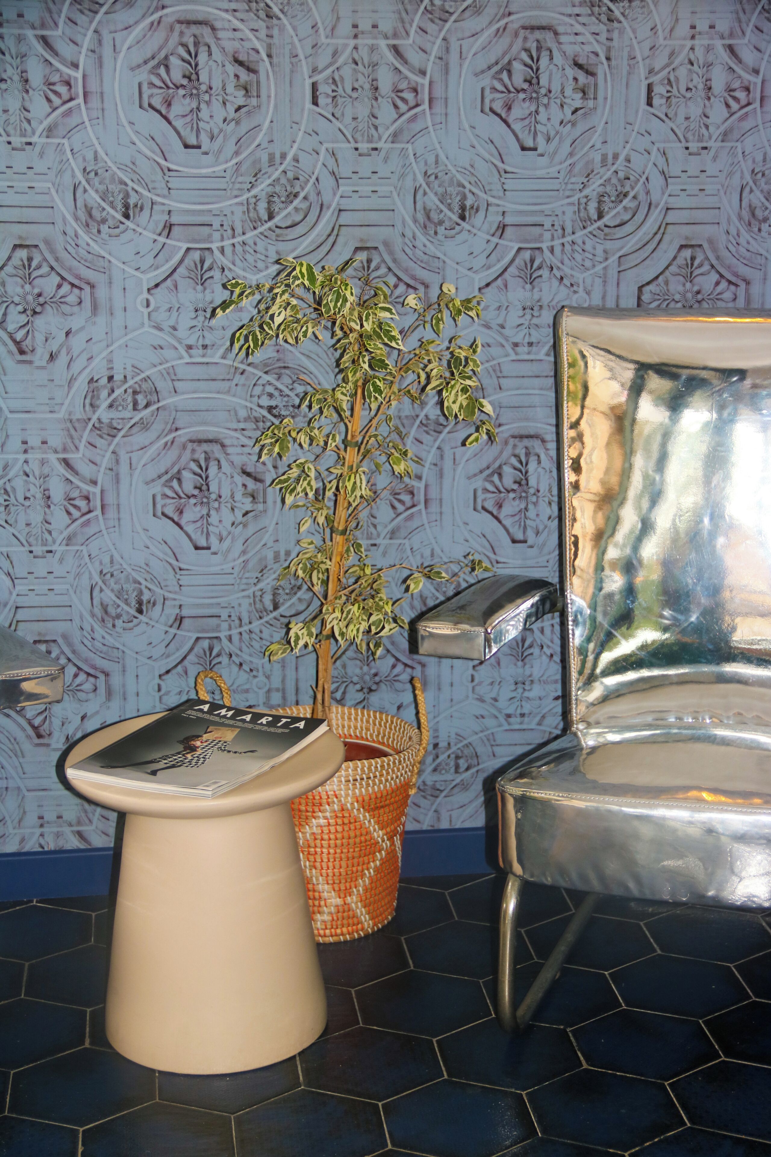 A bathroom with a patterned wall, a sink, a potted plant, and a chrome chair.