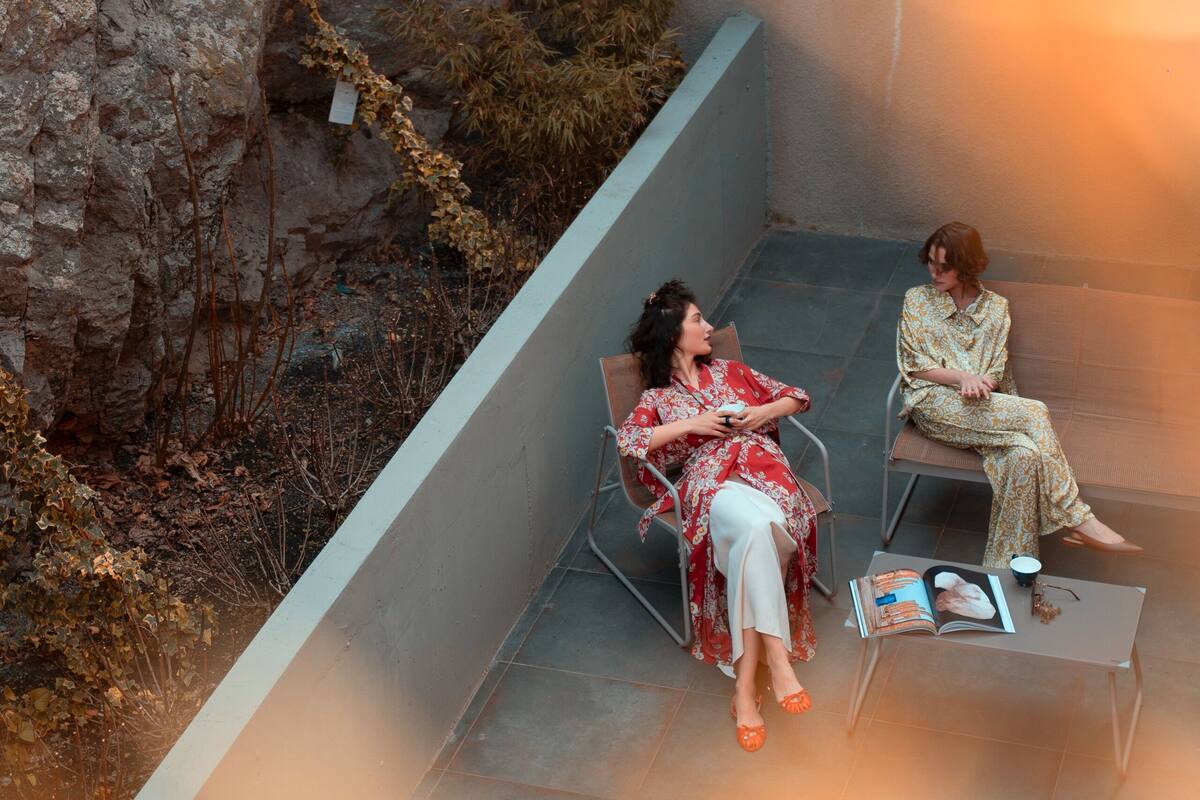 Two people sitting on chairs in an outdoor area with a stone wall and some vegetation.