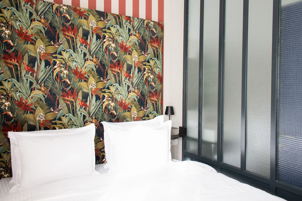 A hotel room with a bed, white pillows, and a tropical wallpaper design.