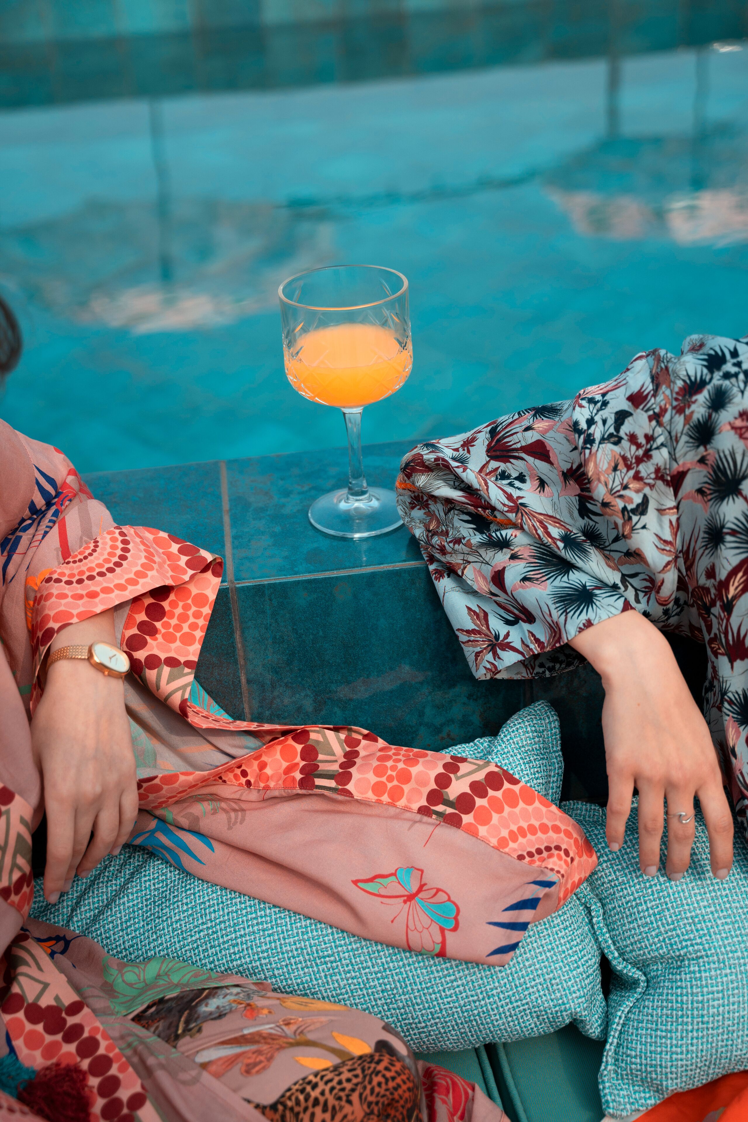 A person sitting by a pool with a glass of orange juice.