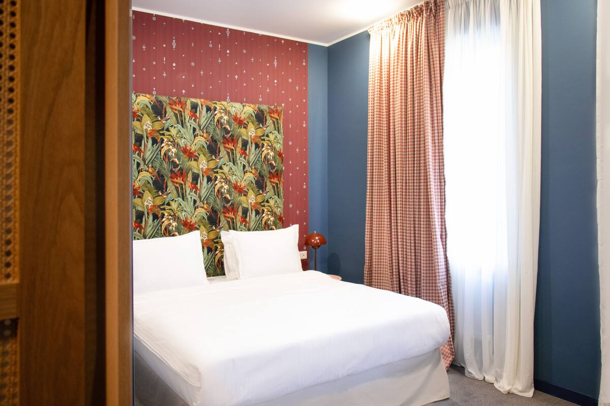 A hotel room with a bed, a nightstand, and a wall with a floral pattern.