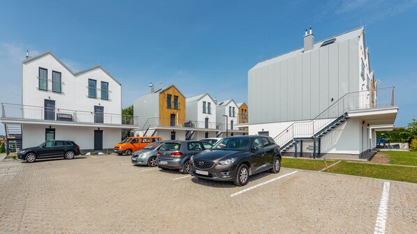 A modern building with multiple units, a parking area with several cars, and a clear sky. - Apartamenty Sun & Snow Wiatrakowo (Wladyslawowo)