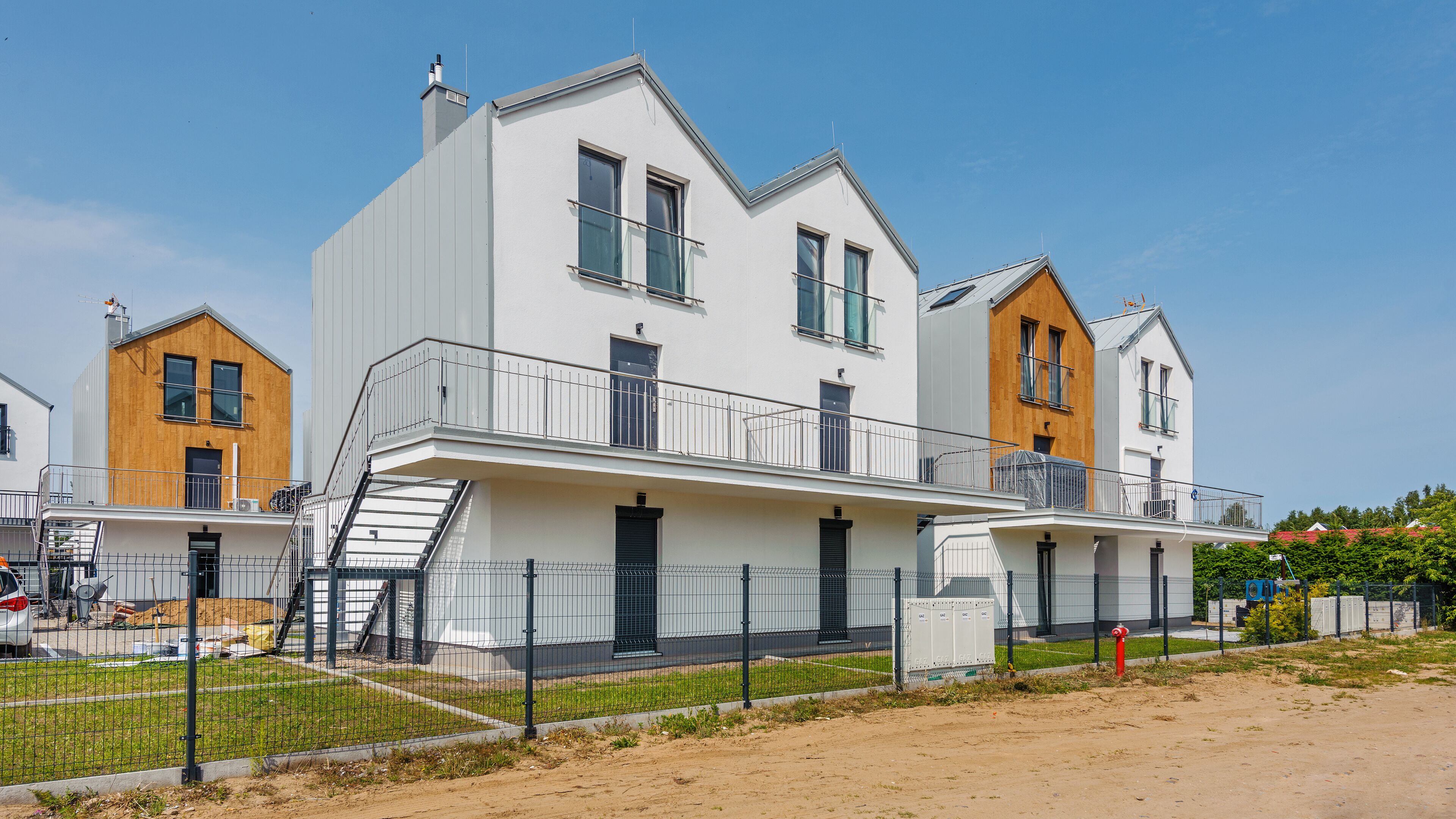 Een modern woonhuis met twee verdiepingen, een balkon, een trap en een omheind erf.