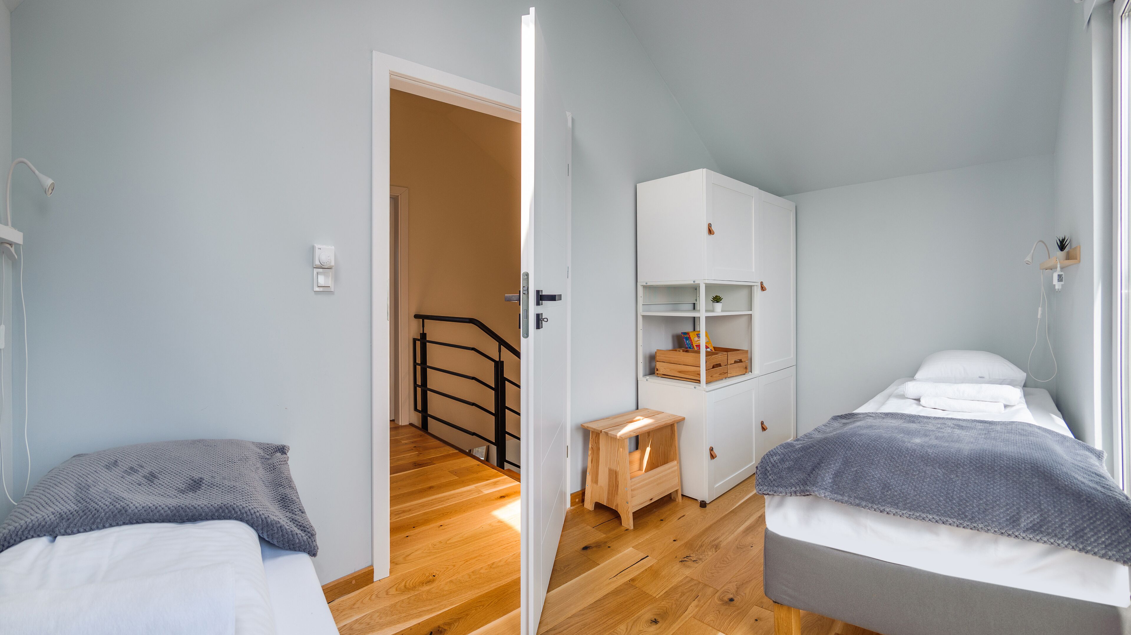 A bedroom with two beds, a wooden bench, a white wardrobe, and a small table with a plant.