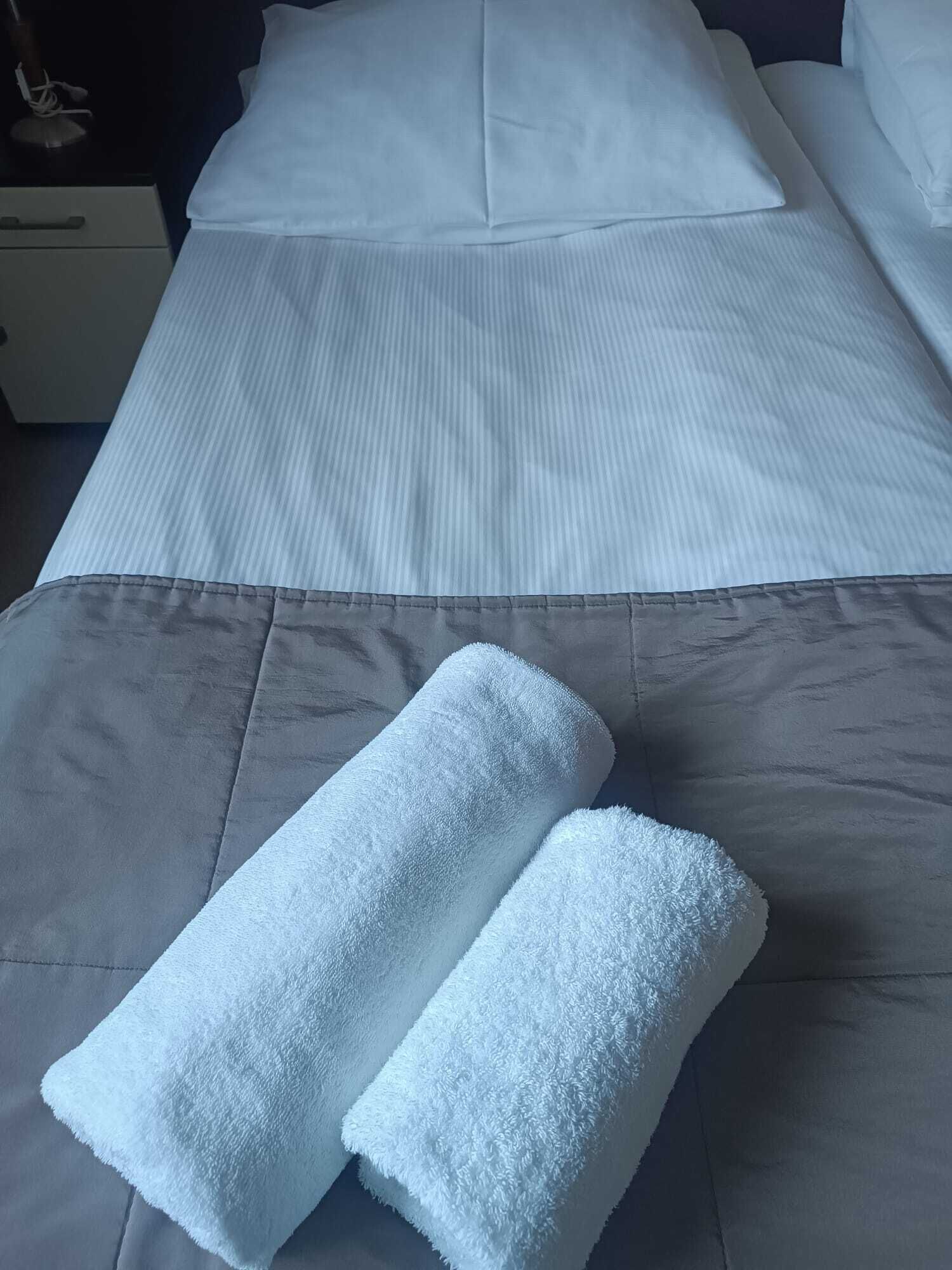 Un lit bien fait, avec des draps blancs et deux serviettes pliées posées sur le lit.