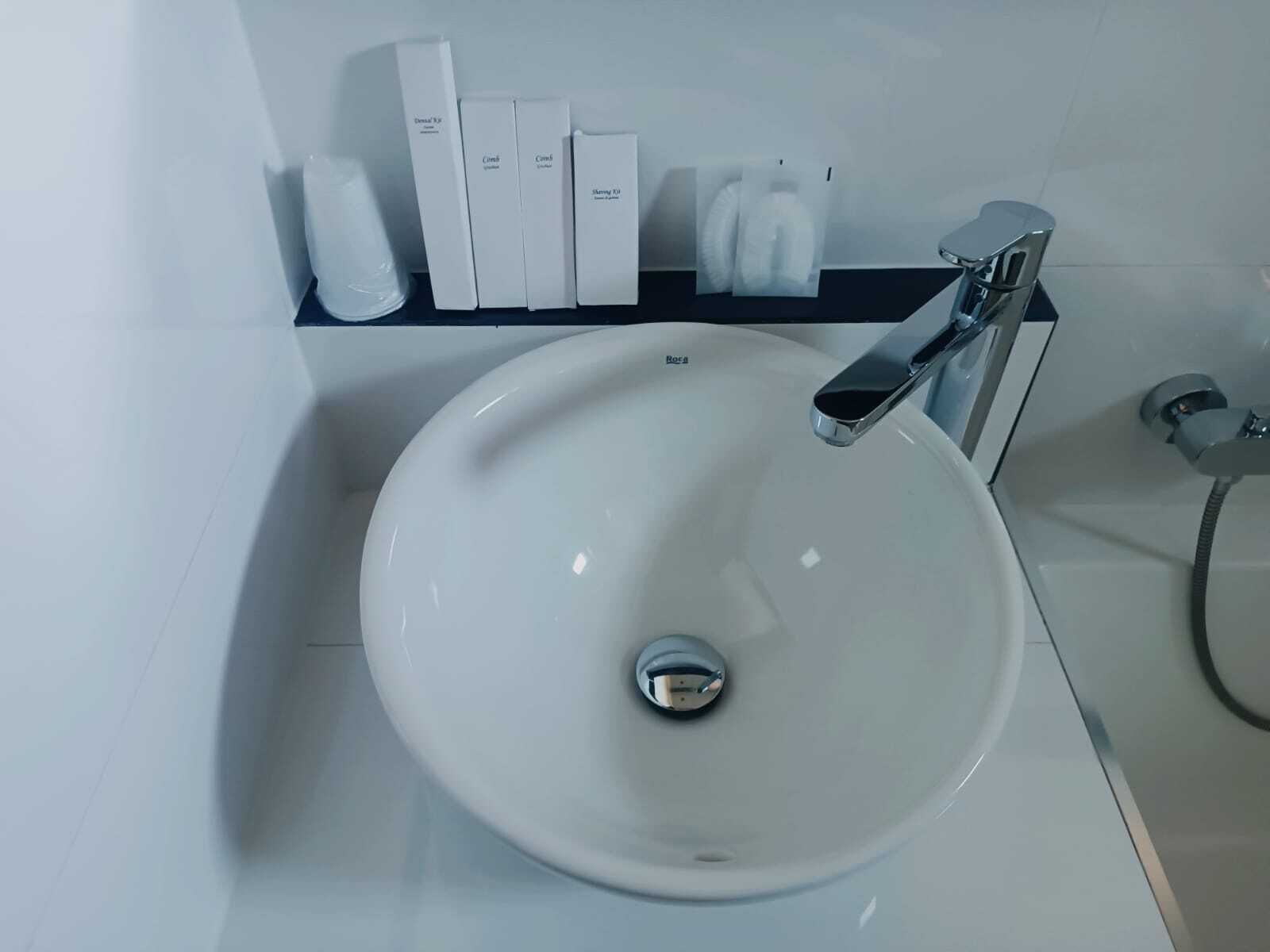 Ein modernes Badezimmer mit einem weißen Waschbecken, einem chromfarbenen Wasserhahn und einem Ablagefach mit Pflegeprodukten.