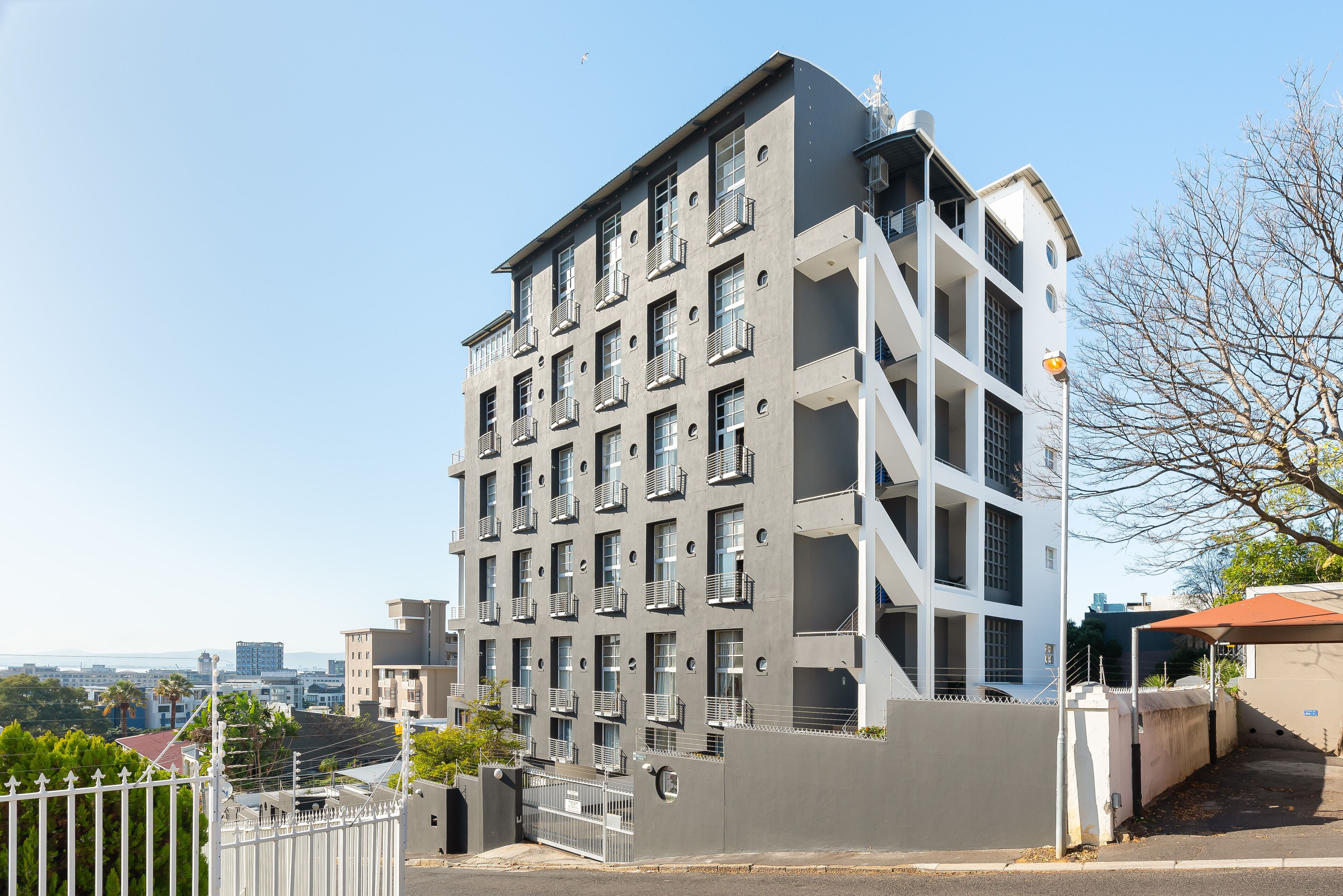 A multi-story residential building with balconies, a gated entrance, and a view of the surrounding area.