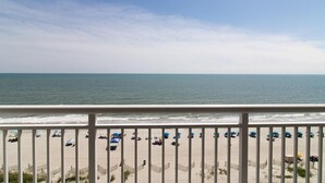 A beach with umbrellas and people, a railing, and the ocean.