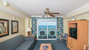 A living room with a sofa, a coffee table, a TV cabinet, and a ceiling fan. - Oceanfront 2 BR Condo Tons of Amenities Low Floor! (Myrtle Beach)