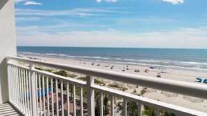 A balcony with a view of a beach with umbrellas and people. - 2 BR Condo Oceanfront Amazing Views 6th Floor! (Myrtle Beach)