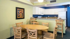 A dining area with a round table and six chairs, a kitchen with white cabinets and a blue accent wall, and a framed picture on the wall. - Oceanfront 2 BR Condo tons of Amenities 9th Floor! (Myrtle Beach)