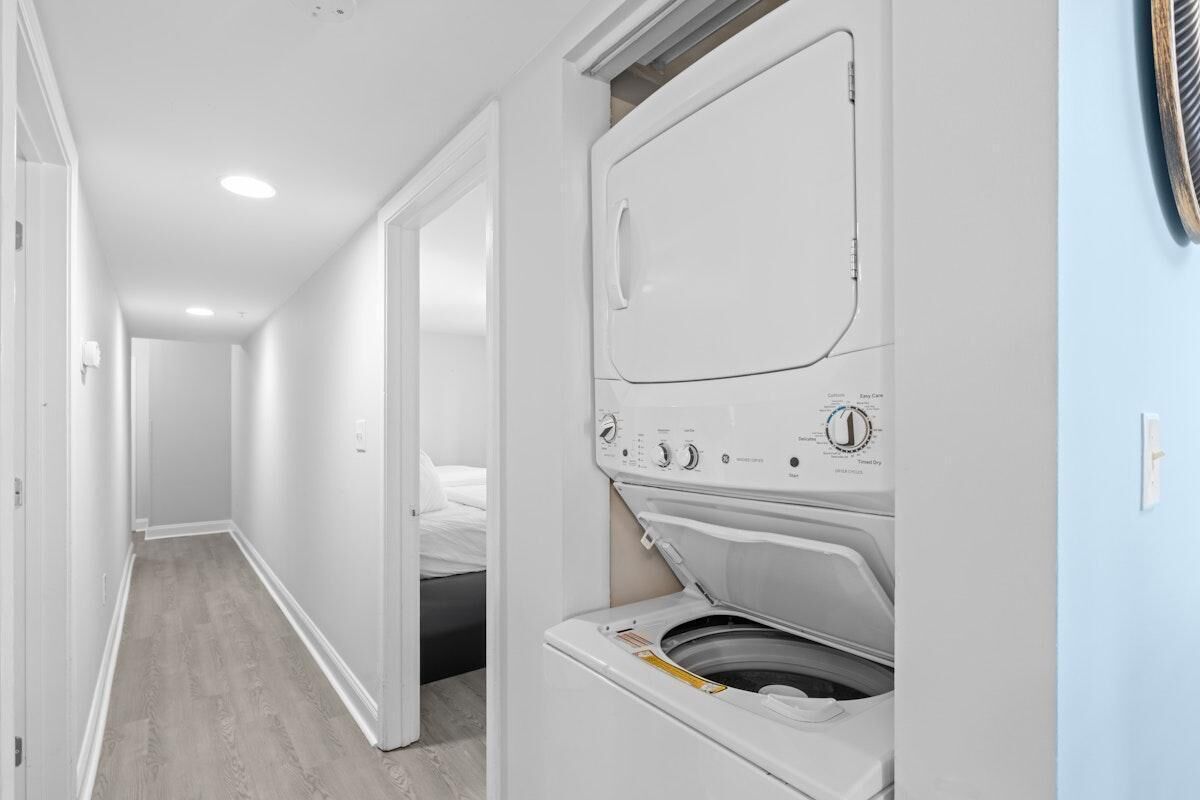 A laundry room with a washer and dryer, a hallway leading to a bedroom, and a door leading to another room.