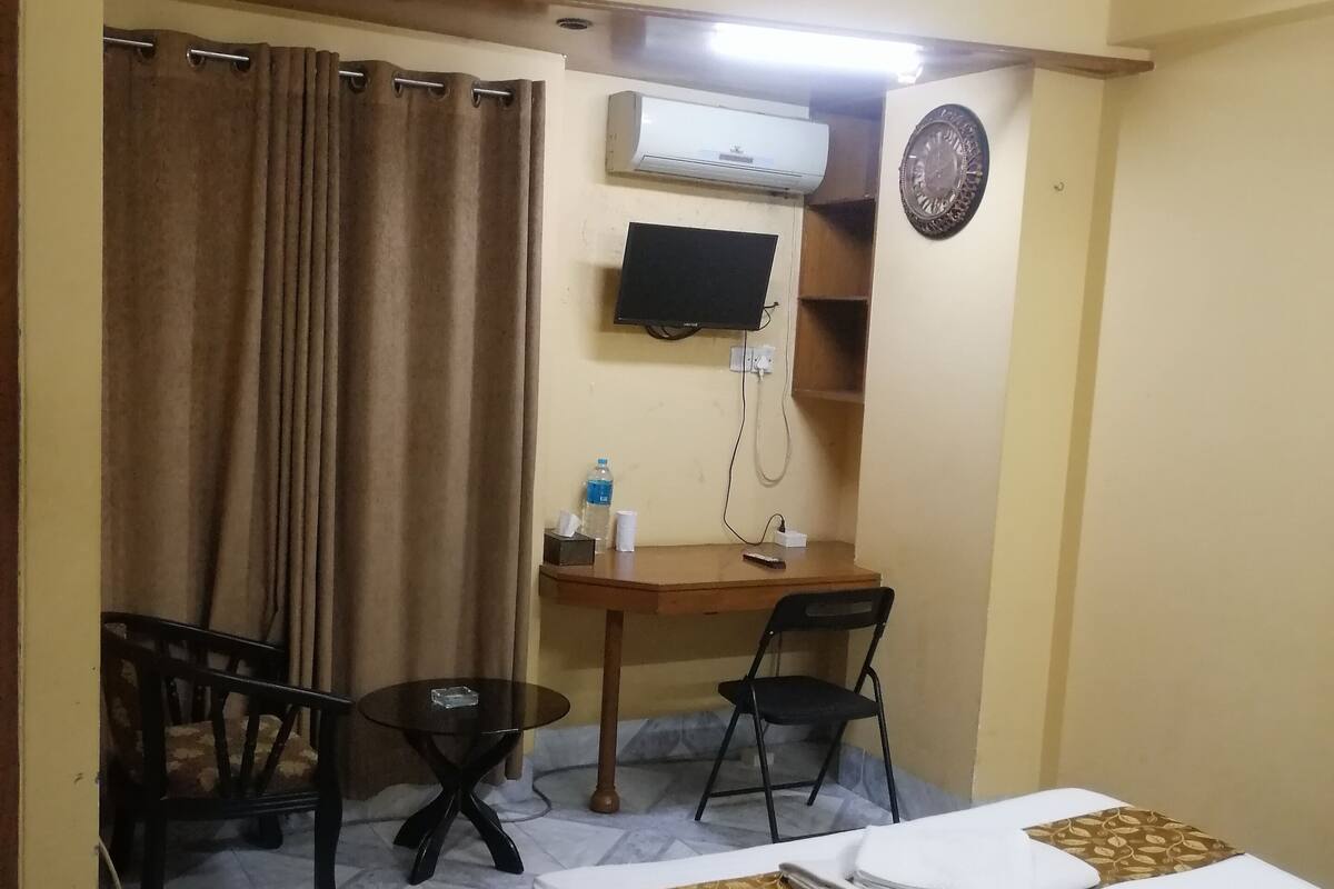 A hotel room with a bed, a desk, a chair, a television, and an air conditioning unit.