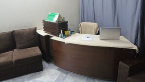 A reception desk with a laptop, a calendar, and some documents. There is a couch and a chair in the room.