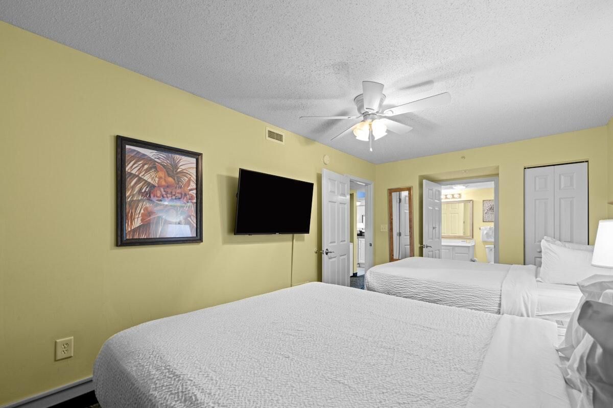 Una camera d'albergo con due letti, una ventola a soffitto, una TV a schermo piatto e un quadro appeso al muro.