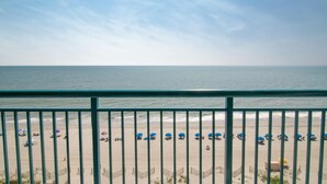 Vista a la playa desde un balcón con barandilla, mostrando una playa de arena con sombrillas y sillas de descanso.