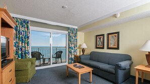 A room with a sofa, a table, a TV, a chair, and a balcony with a view of the sea. - 1BR Oceanfront King Deluxe Condo Unwind 8TH Floor (Myrtle Beach)