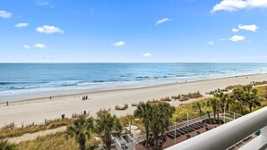 A beach view from a balcony with a clear sky, a sandy beach, and some palm trees. - Coastal Elegance OF King Suite Escape 4th Floor (Myrtle Beach)