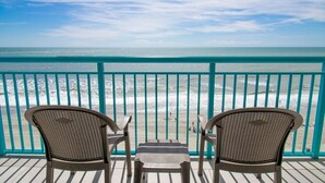 A balcony with two wicker chairs and a small table, overlooking a beach with turquoise water and waves. - Ocean Front King Suite Escape! 7th Floor (Myrtle Beach)