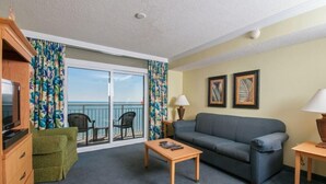 A hotel room with a balcony, a sofa, a coffee table, a TV, and a dresser. - Seaside Serenity1BR Deluxe Condo Low Floor (Myrtle Beach)