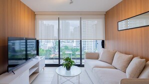 A modern living room with a large flat-screen TV, a sofa, a coffee table, and a balcony with a city view.