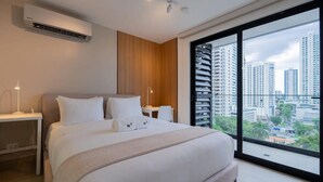 A modern hotel room with a large bed, a nightstand, a bedside table, and a large window offering a city view.