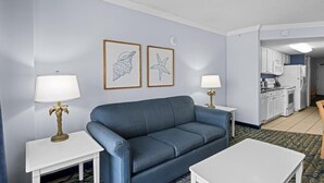 A living room with a blue sofa, white coffee table, and two lamps. There is a kitchen visible in the background. - Gorgeous Oceanfront 1 BR Condo Tons of Amenities (Myrtle Beach)