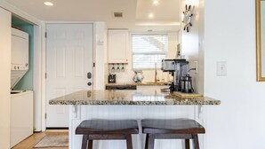 A kitchen with a granite countertop, two barstools, a coffee maker, and a window with blinds. - Boathouse Condo, Waterfront, Golf course, Destin Harbor.  Sandpiper Cove #1055 (Destin)