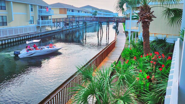 A canal with a boat, a wooden walkway, and a bridge. - Boathouse Condo, Waterfront, Golf course, Destin Harbor.  Sandpiper Cove #1055 (Destin)