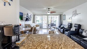 A spacious living area with a large granite floor, a dining table, a sofa, and a TV mounted on the wall. - Boathouse Condo, Waterfront, Golf course, Destin Harbor.  Sandpiper Cove #1055 (Destin)