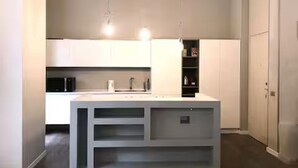 Eine moderne Küche mit weißen Schränken, einer zentralen Kochinsel, Pendelleuchten und einem eingebauten Ofen.