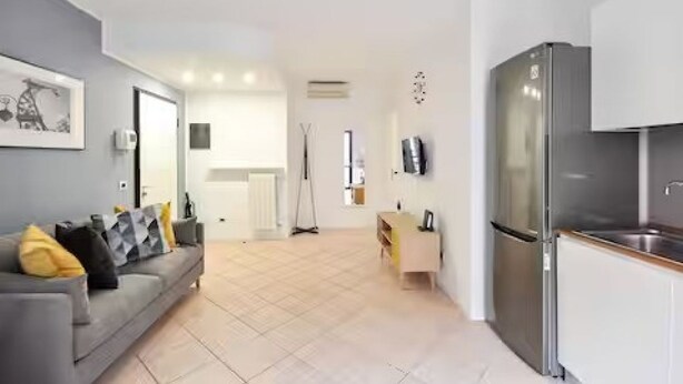 A modern kitchen with a built-in refrigerator, a dining area with a light-colored table, and a gray sofa with cushions. - GuestHost - CASA CRI&ELI: trilo x5 con terrazzo (Milan)