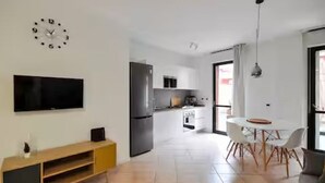 A modern kitchen with a refrigerator, stove, and microwave. There is a dining area with a table and chairs. A flat-screen TV is mounted on the wall. - GuestHost - CASA CRI&ELI: trilo x5 con terrazzo (Milan)