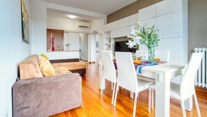 A modern living room with a sofa, dining table, and chairs. There is a kitchen area with cabinets and a refrigerator. - GuestHost - ParkView House! (Milan)