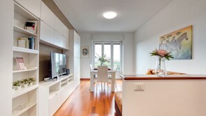 A modern living room with a flat-screen TV, white cabinets, a dining table with chairs, and a painting of zebras. - GuestHost - ParkView House! (Milan)