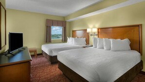 A hotel room with two beds, a TV, a desk, and a window with curtains.