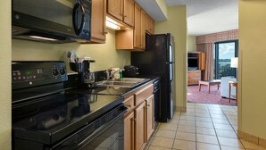 A kitchen with a black stove, wooden cabinets, a black refrigerator, and a window with a view.