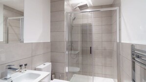 Un baño moderno con ducha de vidrio, un lavamanos blanco y un espejo.