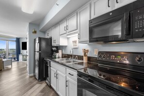 A modern kitchen with white cabinets, a black refrigerator, a microwave, and a stove.