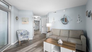 Uma sala de estar com sofá, mesa de centro, poltrona estampada e decoração náutica.