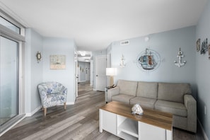 Un salón con sofá, una mesa de centro, un sillón estampado y decoración náutica.