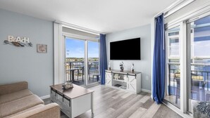 Uma sala de estar moderna com televisão de tela plana, um sofá, uma mesa de jantar e uma varanda com vista.
