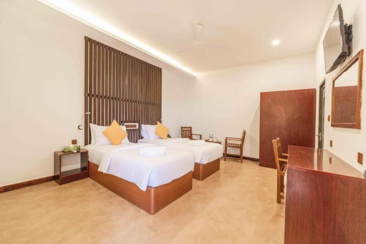 A hotel room with two beds, a desk, a chair, a wardrobe, and a ceiling fan.