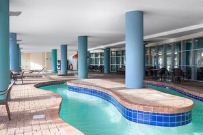 An indoor swimming pool with blue-tiled edges, surrounded by blue pillars and a brick floor. - Attractive Oceanfront Condo at Bay View Resort (Myrtle Beach)